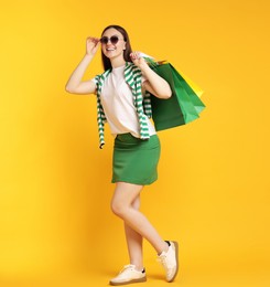 Photo of Positive woman with shopping bags on yellow background