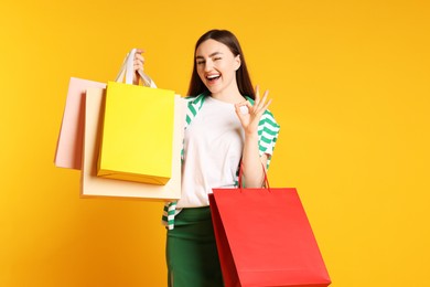 Photo of Excited woman with shopping bags showing okay gesture on yellow background