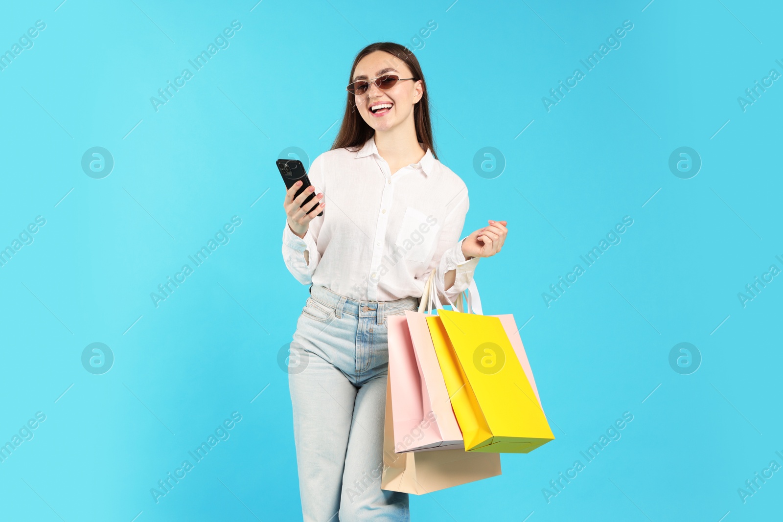 Positive woman with smartphone and shopping bags on light blue background Photo of Positive woman with smartphone and shopping bags on light blue background