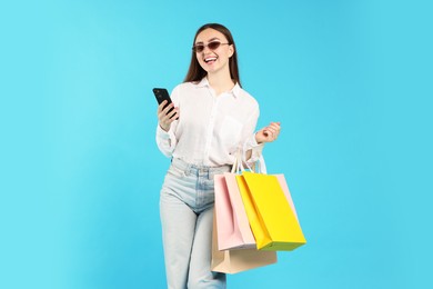 Photo of Positive woman with smartphone and shopping bags on light blue background