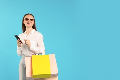 Photo of Positive woman with smartphone and shopping bags on light blue background. Space for text