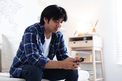 Photo of Handsome Asian man with smartphone on sofa at home