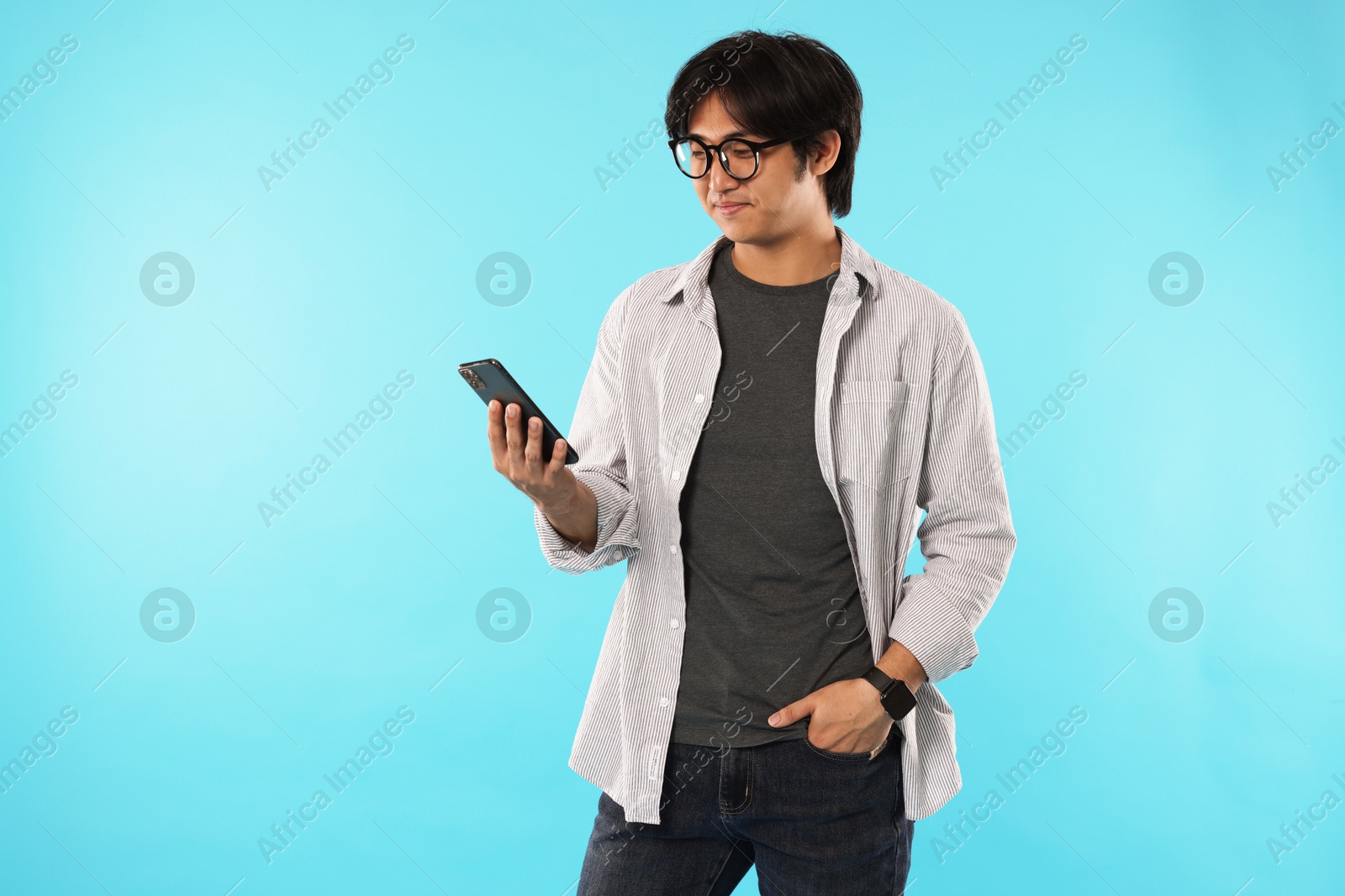 Handsome Asian man with smartphone on light blue background Photo of Handsome Asian man with smartphone on light blue background