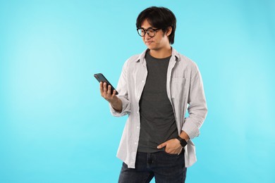 Photo of Handsome Asian man with smartphone on light blue background