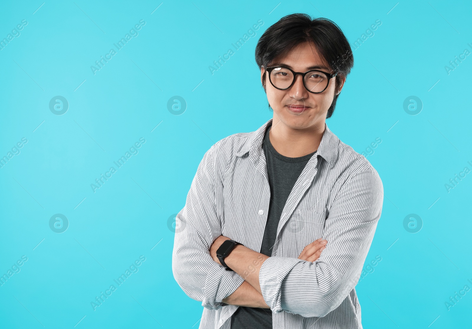 Handsome Asian man in glasses with crossed arms on light blue background. Space for text Photo of Handsome Asian man in glasses with crossed arms on light blue background. Space for text