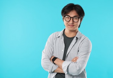Photo of Handsome Asian man in glasses with crossed arms on light blue background. Space for text
