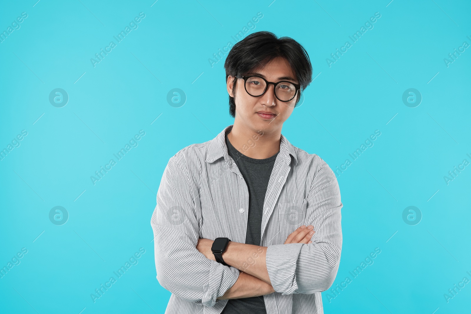 Photo of Handsome Asian man in glasses with crossed arms on light blue background