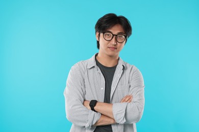Photo of Handsome Asian man in glasses with crossed arms on light blue background