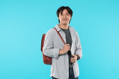 Photo of Handsome Asian man with laptop and backpack on light blue background