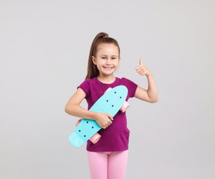 Photo of Little girl with penny board showing thumbs up on light grey background