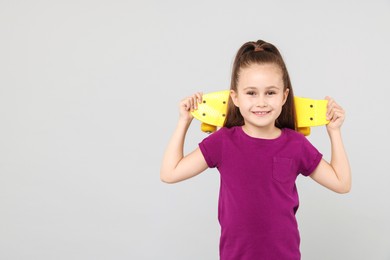 Photo of Little girl with penny board on light grey background, space for text
