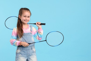 Photo of Little girl with tennis rackets on light blue background, space for text