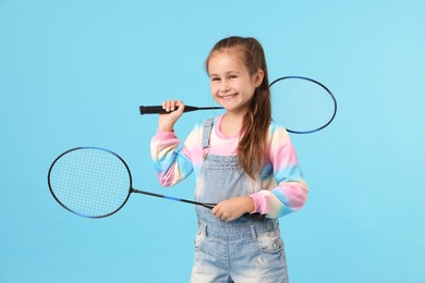 Photo of Little girl with tennis rackets on light blue background
