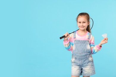 Photo of Little girl with tennis racket and shuttlecock on light blue background, space for text