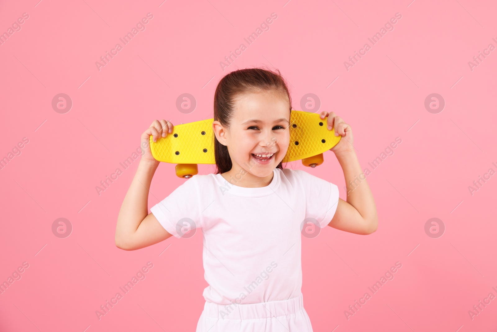 Little girl with penny board on pink background Photo of Little girl with penny board on pink background