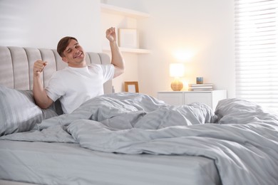 Photo of Young man stretching on bed with soft mattress at home
