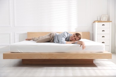 Photo of Young man lying on bed with soft mattress at home