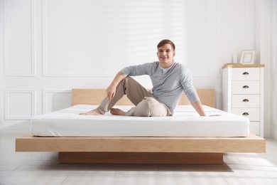 Photo of Young man sitting on bed with soft mattress at home