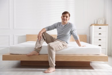 Photo of Young man sitting on bed with soft mattress at home