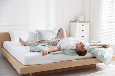 Photo of Young man lying on bed with soft mattress at home