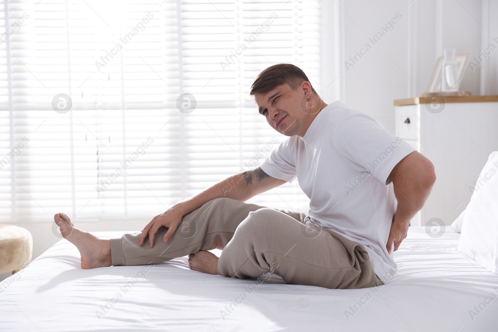 Young man suffering from back pain on bed with soft mattress at home Photo of Young man suffering from back pain on bed with soft mattress at home