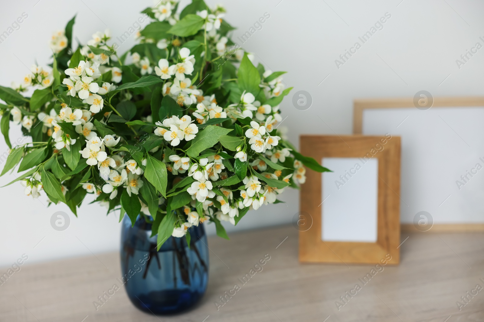Beautiful jasmine flowers in vase and photo frames on wooden table indoors, closeup Photo of Beautiful jasmine flowers in vase and photo frames on wooden table indoors, closeup