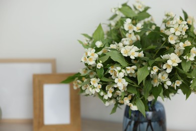 Photo of Beautiful jasmine flowers in vase and photo frames on table indoors, closeup. Space for text