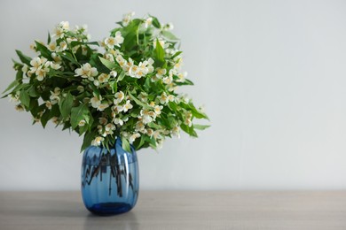 Photo of Beautiful jasmine flowers in vase on table indoors, space for text