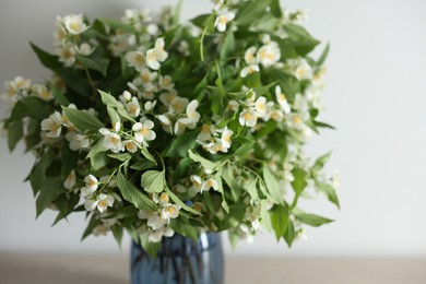 Photo of Beautiful jasmine flowers in vase on table indoors, closeup