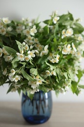 Photo of Beautiful jasmine flowers in vase on table indoors, closeup