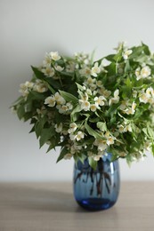 Photo of Beautiful jasmine flowers in vase on table indoors, closeup