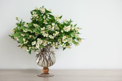 Photo of Beautiful jasmine flowers in vase on wooden table indoors, space for text