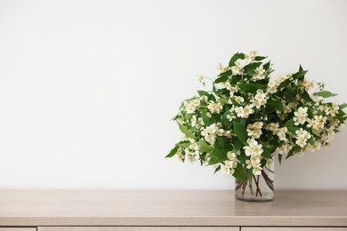 Photo of Beautiful jasmine flowers in vase on wooden table indoors, space for text