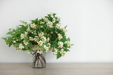 Photo of Beautiful jasmine flowers in vase on wooden table indoors, space for text