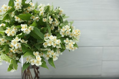 Photo of Beautiful jasmine flowers in vase near white wooden wall indoors, closeup. Space for text