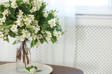 Photo of Beautiful jasmine flowers in vase on table indoors, space for text