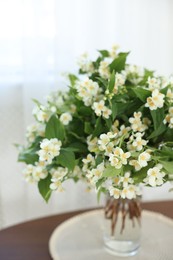 Photo of Beautiful jasmine flowers in vase on table indoors, closeup