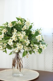 Photo of Beautiful jasmine flowers in vase on table indoors