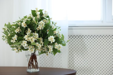 Photo of Beautiful jasmine flowers in vase on table indoors, space for text