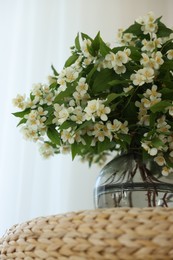 Photo of Beautiful jasmine flowers in vase on wicker table indoors, low angle view