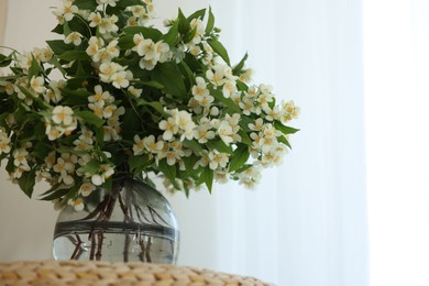 Photo of Beautiful jasmine flowers in vase on wicker table indoors, low angle view. Space for text