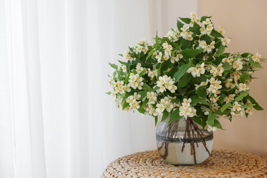 Photo of Beautiful jasmine flowers in vase on wicker table near window indoors, space for text
