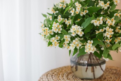 Photo of Beautiful jasmine flowers in vase on wicker table near window indoors, closeup. Space for text