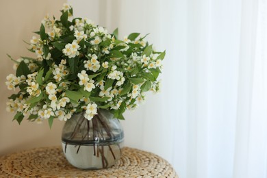 Photo of Beautiful jasmine flowers in vase on wicker table near window indoors, space for text