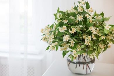 Photo of Beautiful jasmine flowers in vase on white table near window, closeup. Space for text