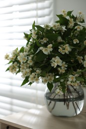 Photo of Beautiful jasmine flowers in vase on table near window indoors, closeup
