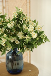 Photo of Beautiful jasmine flowers in vase on wooden table indoors, closeup