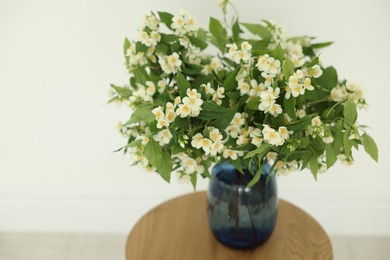 Photo of Beautiful jasmine flowers in vase on wooden table near white wall indoors, closeup. Space for text