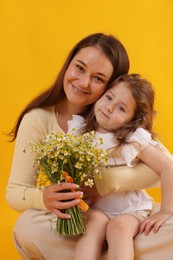 Photo of Mother and her little daughter with bouquet of beautiful chamomile flowers on orange background