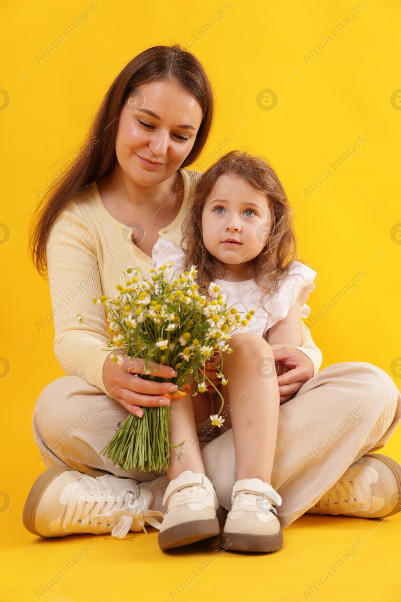 Mother and her little daughter with bouquet of beautiful chamomile flowers on orange background Photo of Mother and her little daughter with bouquet of beautiful chamomile flowers on orange background
